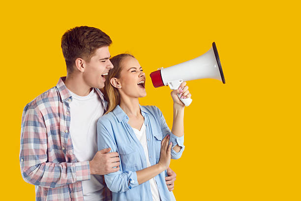istock Funny joyful young couple with loudspeaker making loud advertisement on orange background. 2249023606