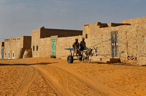 Chinguetti, Mauritania. October 04, 2021. Two Africans in national clothes are leisurely walking in a donkey cart along a sandy city street.