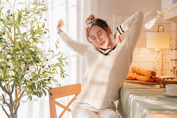 woman greets the good morning, stretching her arms by the window during a relaxing weekend breakfast. This moment captures a healthy home routine and wellness lifestyle