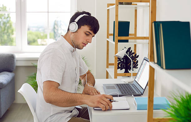 istock Young man working in his home office, sitting at desk, using laptop and writing in notebook 2249031229