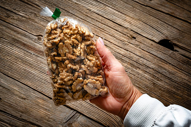 Female hand holding a plastic bag filled with freshly peeled organic walnuts shot on rustic wooden table background. Healthy food or nut