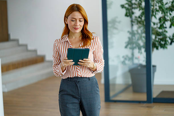 istock Businesswoman walking in modern office corridor using digital tablet for remote work and communication 2249039182