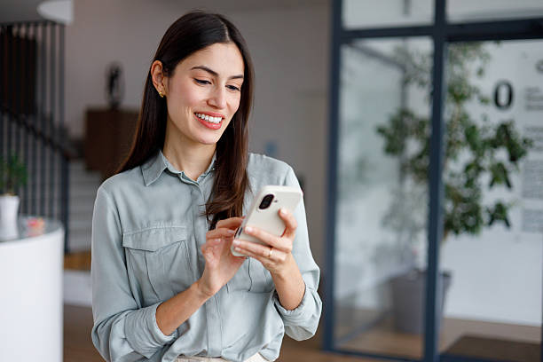 istock Professional businesswoman smiling while sending text messages on smartphone at modern workplace 2249039663