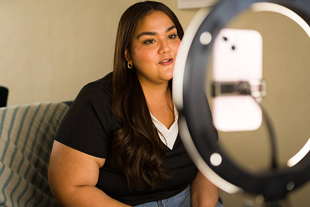 istock Plus-size woman creating online video content with a smartphone and ring light, vlogging for her social media channel 2249042242