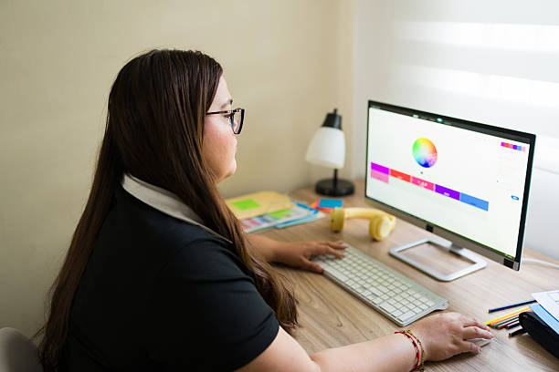 istock Young adult woman designing a digital project, choosing colors and working on her computer from a home office desk 2249043400