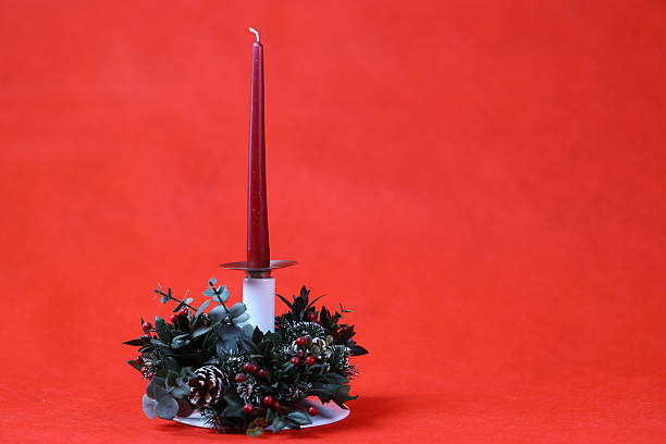 Close-up view of a festive table setting featuring a decorative candle holder on a reflective tray, with red chili peppers and citrus fruits arranged on a textured tablecloth, illuminated by warm indoor lighting.