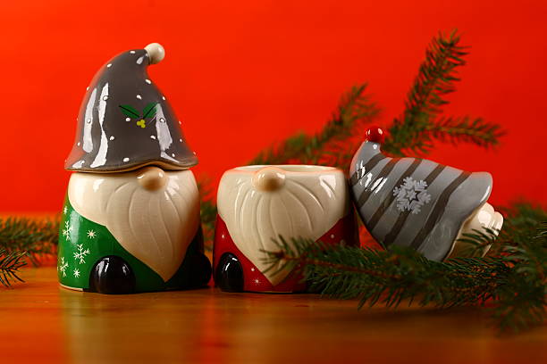 Two charming ceramic Christmas gnomes displayed among spruce branches and red ornaments. Their painted hats and cheerful faces capture the magic of the holiday season. The strong red background adds a vibrant Christmas feel, making the image ideal for seasonal marketing, decorations, and festive print materials.