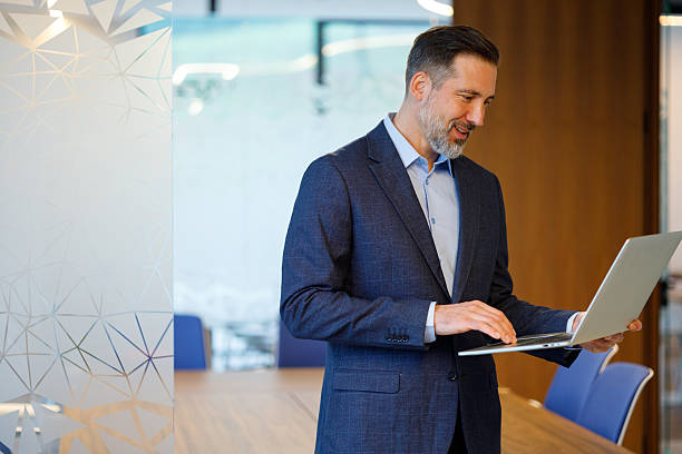 istock Mid adult man using a laptop, looking at the screen and typing. Modern office interior with frosted glass and meeting table 2249052767