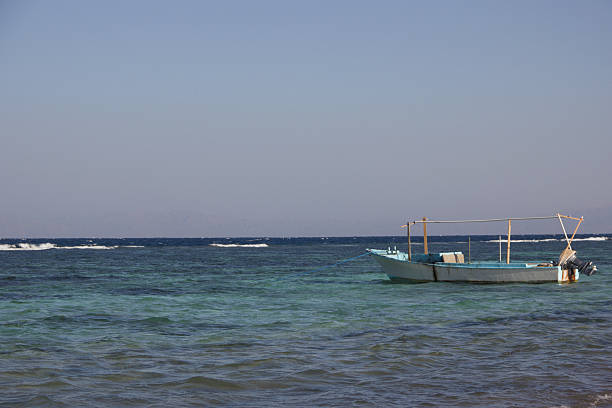 Traditional fishing boat anchored on the clear Red Sea coast in Egypt, with calm turquoise water and distant desert mountains. Natural travel and marine background suitable for tourism, adventure, and coastal themes.