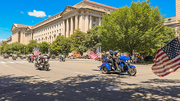 Washington D.C., USA, May 25, 2025. A blue three-wheeled motorcycle with American flags rides by during a Memorial Day parade.
