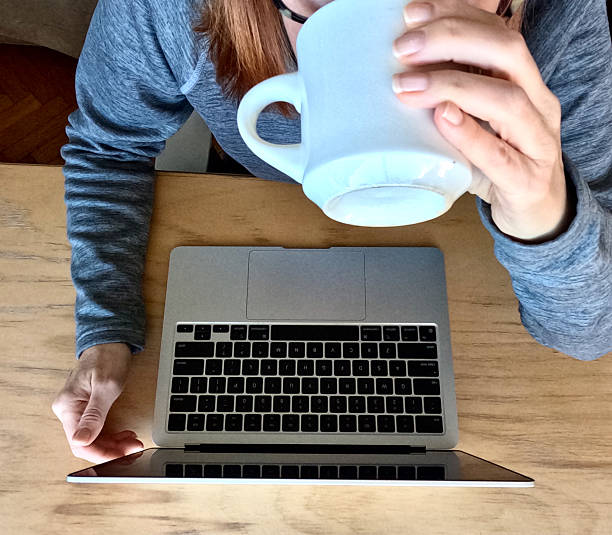 EX high angle MS woman drinking coffee while working on laptop at office desk