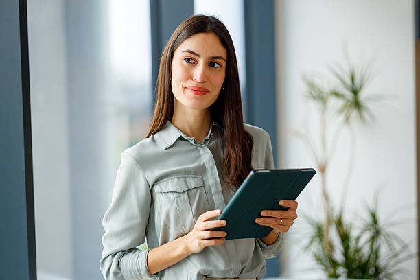 istock Confident businesswoman smiling while holding a digital tablet, looking away, thinking about business success 2249069059