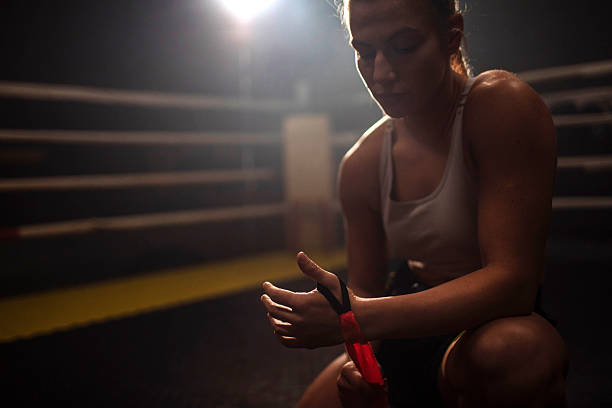 Athlete in a white sports bra adjusts a wrist wrap, focused before training in moody lighting