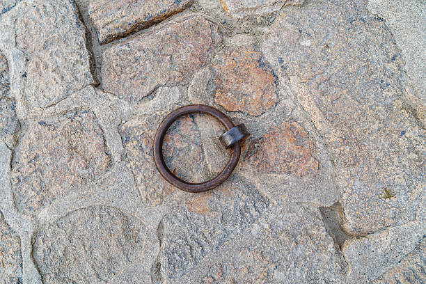 A rusty metal ring is sitting on a stone surface. The ring is old and worn, and it is a piece of jewelry. The stone surface is rough and uneven, giving the scene a sense of age and history.