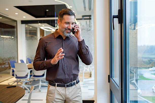 istock Businessman on phone call, smiling while standing in modern office near window, communicating with clients 2249089499