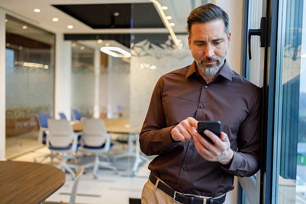 istock Experienced businessman utilizing a smartphone while standing beside a window in a modern corporate office setting 2249089500