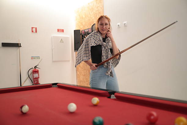 Woman standing by a red pool table holding a cue and contemplating the next move