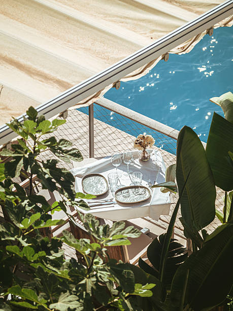 Elegant dining table set under a canopy on a seaside terrace in Nice, France, surrounded by lush greenery and overlooking the sparkling blue Mediterranean Sea.