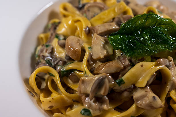 Close-up capture of creamy mushroom tagliatelle pasta featuring sautéed mushrooms, fresh herbs, and a crispy basil leaf on top. The warm tones and rich textures highlight the comforting nature of classic Italian cuisine, ideal for restaurant menus, cooking blogs, and gourmet food stock photography.