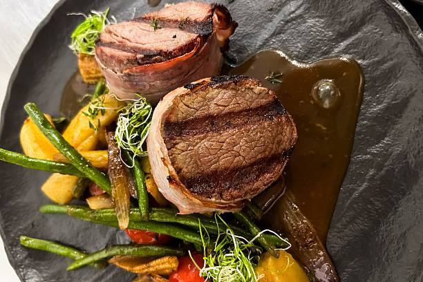 A beautifully plated grilled meat dish features tender juicy portions of beef with grill marks accompanied by vibrant fresh vegetables and rich sauce. Perfect for a gourmet dining experience.