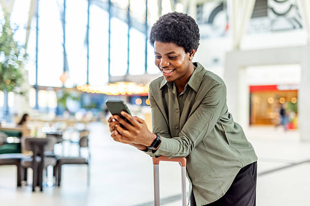 istock Smiling Woman Using Smartphone While Leaning on Luggage in Modern Indoor Space 2249099664