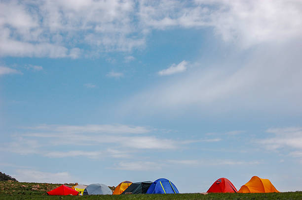 Colorful tents are pitched on a grassy area under a bright blue sky with scattered clouds.