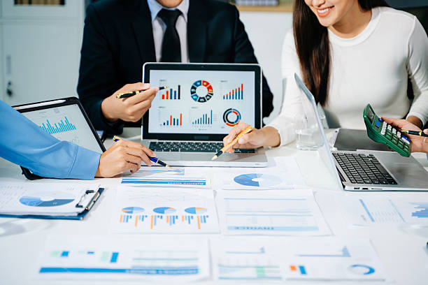 istock Business documents on office table with smart phone and laptop and two colleagues discussing data in the background 2249124064