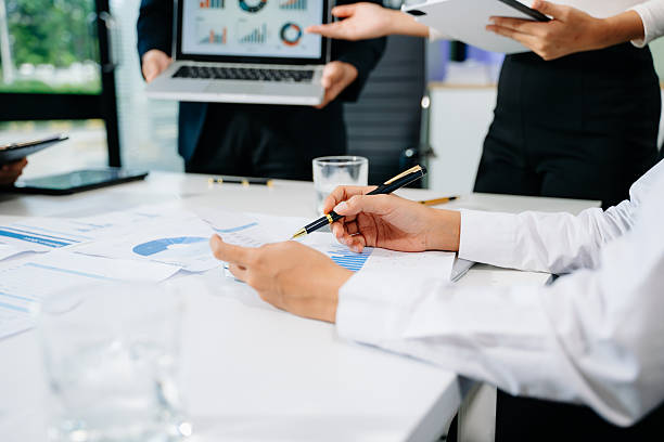 istock Business documents on office table with smart phone and laptop and two colleagues discussing data in the background 2249124086