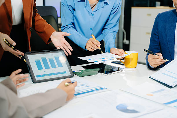istock Business documents on office table with smart phone and laptop and team colleagues discussing data 2249124110