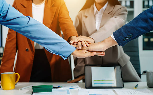 Young Asian business team joins hands in unity, symbolizing teamwork, collaboration, and success in a modern office. Perfect for business, motivation, and leadership themes.