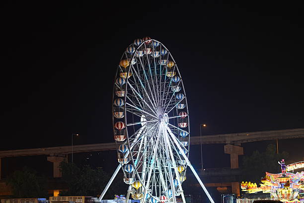 A mesmerizing Ferris wheel stands illuminated at night, surrounded by vibrant carnival lights, creating a lively and festive atmosphere perfect for outdoor events.