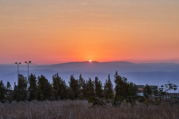 Sunset over misty mountains with warm orange sky and dry field in foreground, creating peaceful and cinematic evening view.