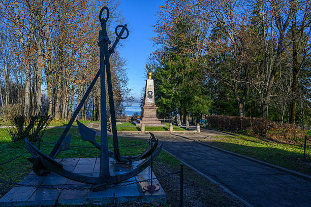 People driving near the anchor monument in Tivat. It marks the centenary of the Naval Arsenal (1889–1989), a shipyard established by the Austro-Hungarian Empire and later central to the Yugoslav Navy. The plaque also references the Mornaričko-Tehnički Remontni Zavod “Sava Kovačević”, the naval overhaul institute named after Sava Kovačević (1905–1943), a celebrated Montenegrin Partisan commander killed in WWII. The site highlights Tivat’s long-standing maritime and naval heritage.