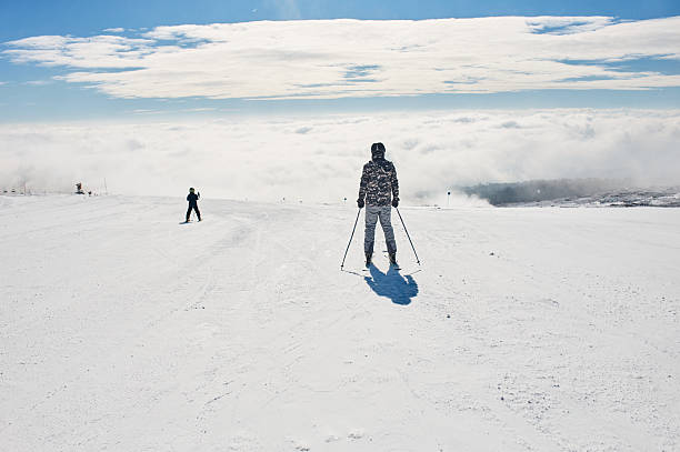Skiers enjoying a sunny day on a snow-covered mountain with clouds covering the valley
