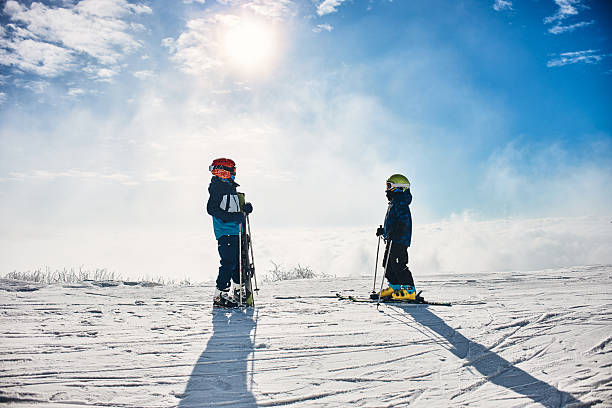 Children wearing ski gear standing on a snowy mountain enjoying winter sports