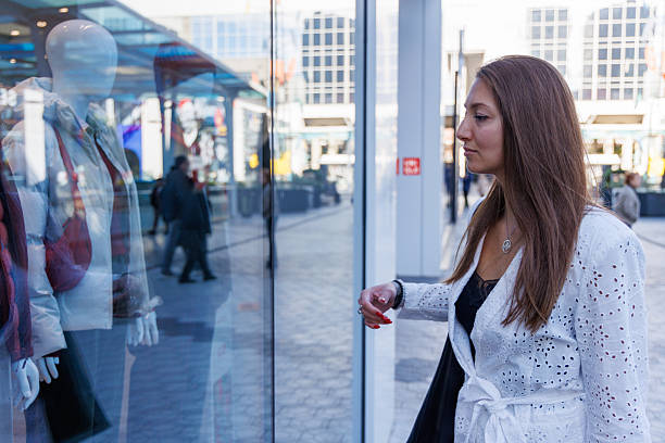 istock Chic female model pausing at a glass storefront inside a busy shopping center during her shopping day 2249132210