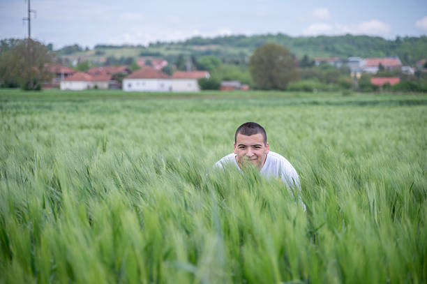 The young man is in the field of cereals, where he observes whether there is any success. The field is flat and small hills can be seen in the background.