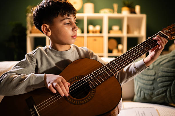 istock Young boy concentrating on learning acoustic guitar at home 2249138984
