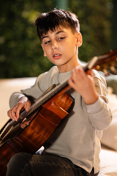 istock Boy playing acoustic guitar concentrating on music practice 2249139009