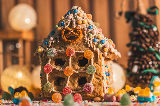 Warm festive composition of a homemade gingerbread house, jelly candies and glowing bokeh tree lights. Soft Christmas charm and sweet seasonal spirit.