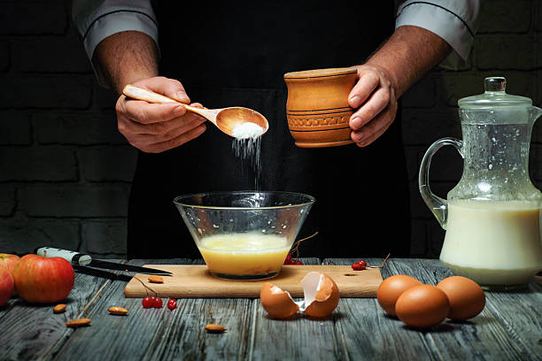 istock A person is pouring sugar from a small container into a glass bowl filled with egg mixture. Surrounding are fresh apples, eggs, and a pitcher of milk on a wooden table 2249154845