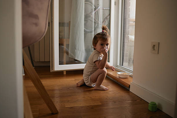 istock Toddler girl holding pacifier crouching by window 2249159251