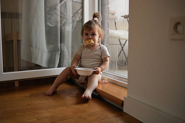 istock Adorable baby eating snack sitting by window 2249159387