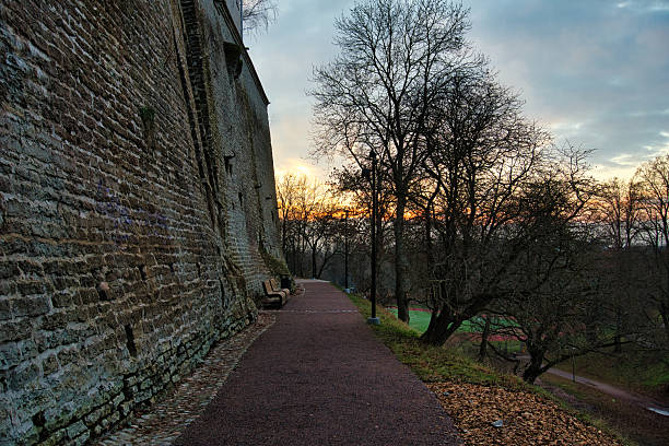 Discover Tallinn's historic embrace as sunset casts a golden glow on the ancient Toompea castle wall and tranquil pathway.