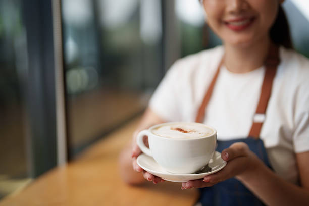 Barista holding a fresh hot cappuccino with latte art, ready to serve a customer, showcasing excellent service and hospitality in a modern coffee shop