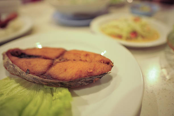 Fried Spanish mackerel with fish sauce, golden crispy surface, served on a white plate, authentic Thai home-style cuisine
