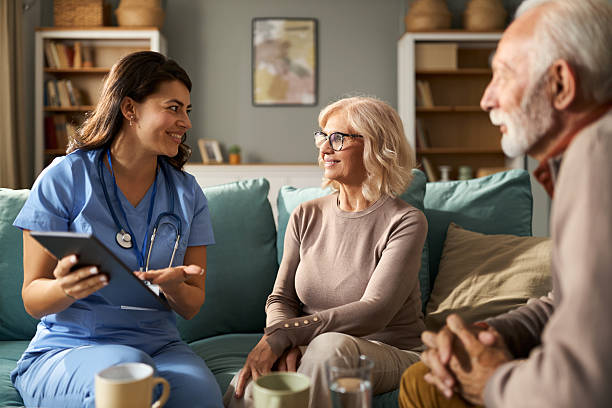 istock Female caregiver using touchpad with senior couple during home visit 2249195936