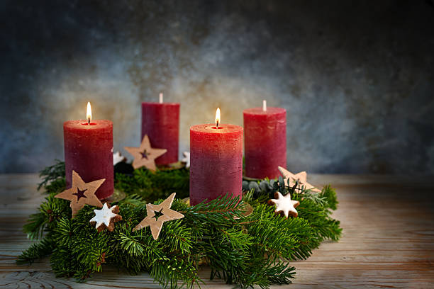 Four red candles on an Advent wreath, two are lit for the second advent, small stars and cinnamon cookies as Christmas decoration, bluish background, copy space, selected focus