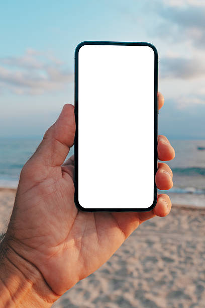 istock Hand holding smartphone with blank screen on beach at sunset, showcasing apps, web design, or UI in natural outdoor setting. 2249198192