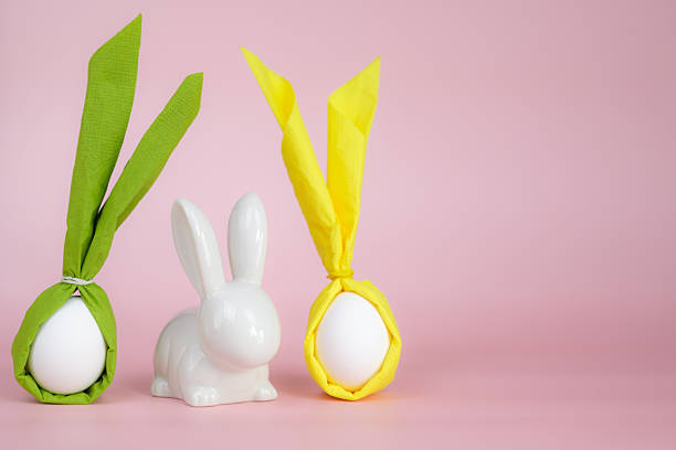 istock Easter composition with a white decorative bunny and eggs decorated in the form of bunnies with napkin ears on a pink background. Spring holiday decor. 2249199424